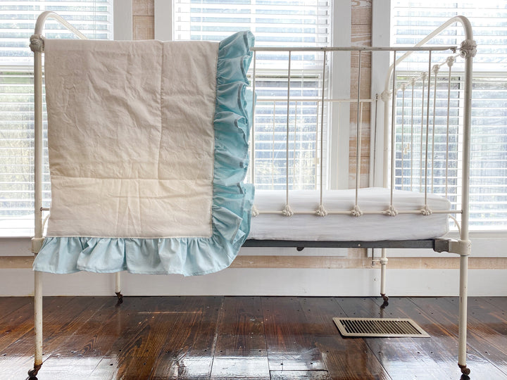 Ivory and mist ruffled baby quilt hung over the end of an antique white iron crib