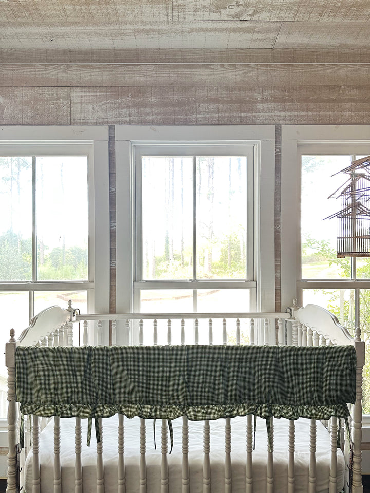 Pine green gingham ruffled crib rail cover on the front rail of a white spindle crib