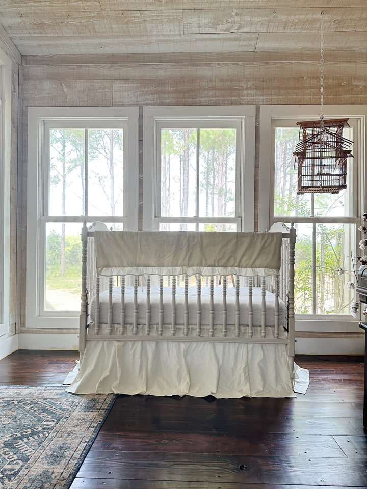 Porcelain crib bedding set styled beneath three windows in a pine-panelled nursery