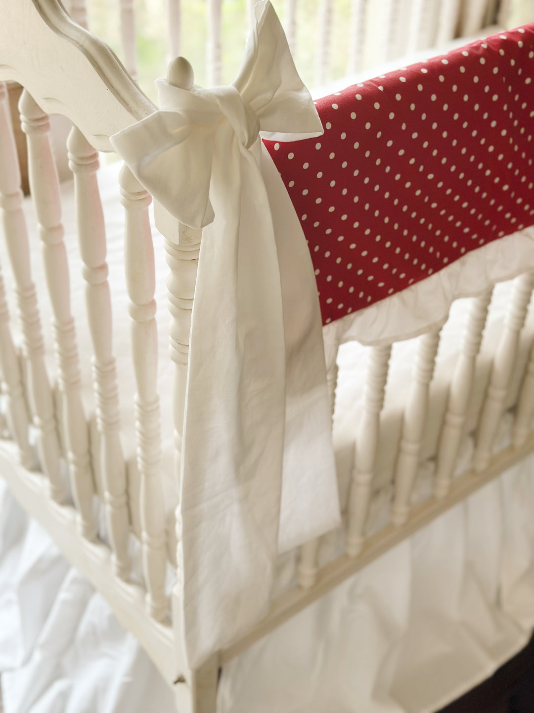 Large white bow knotted over the crib finial beside the red polka dot rail cover