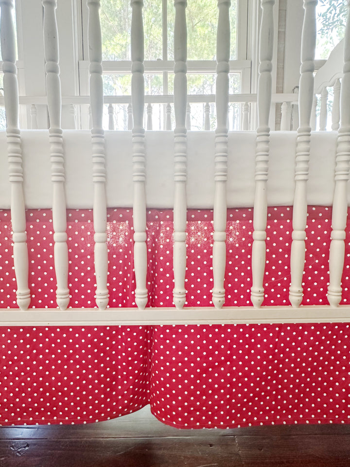 The skirt filling the frame through the crib spindles — small white dots and the inverted center pleat