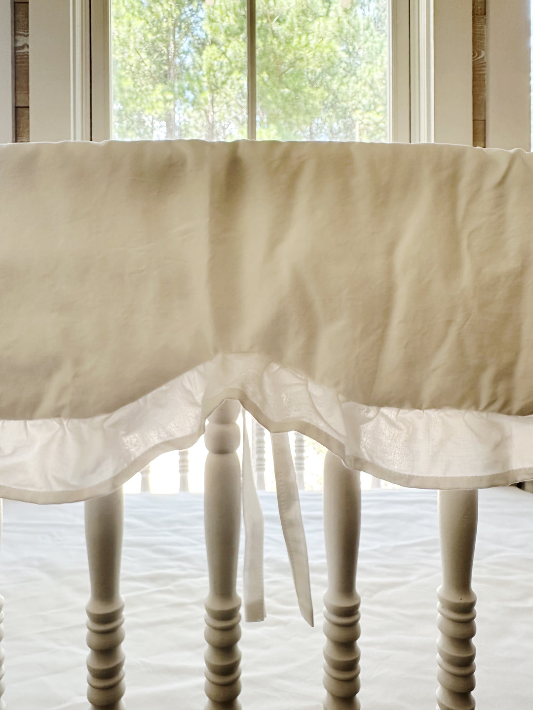 Close-up of the scalloped edge and ruffle trim on the white cotton crib rail cover