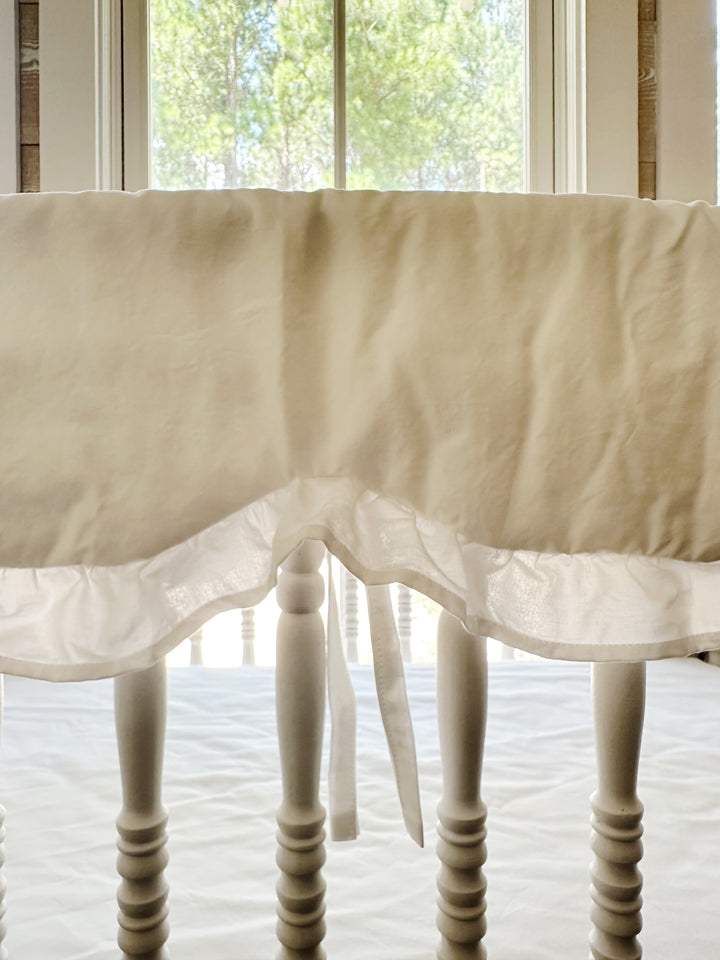 Close-up of the scalloped edge and ruffle trim on the white cotton crib rail cover