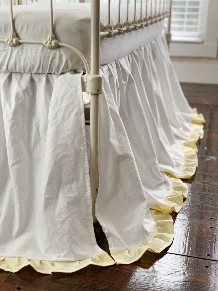 Side close-up of white gathered crib skirt with baby yellow ruffle trim on iron crib, long drop, handmade nursery bedding