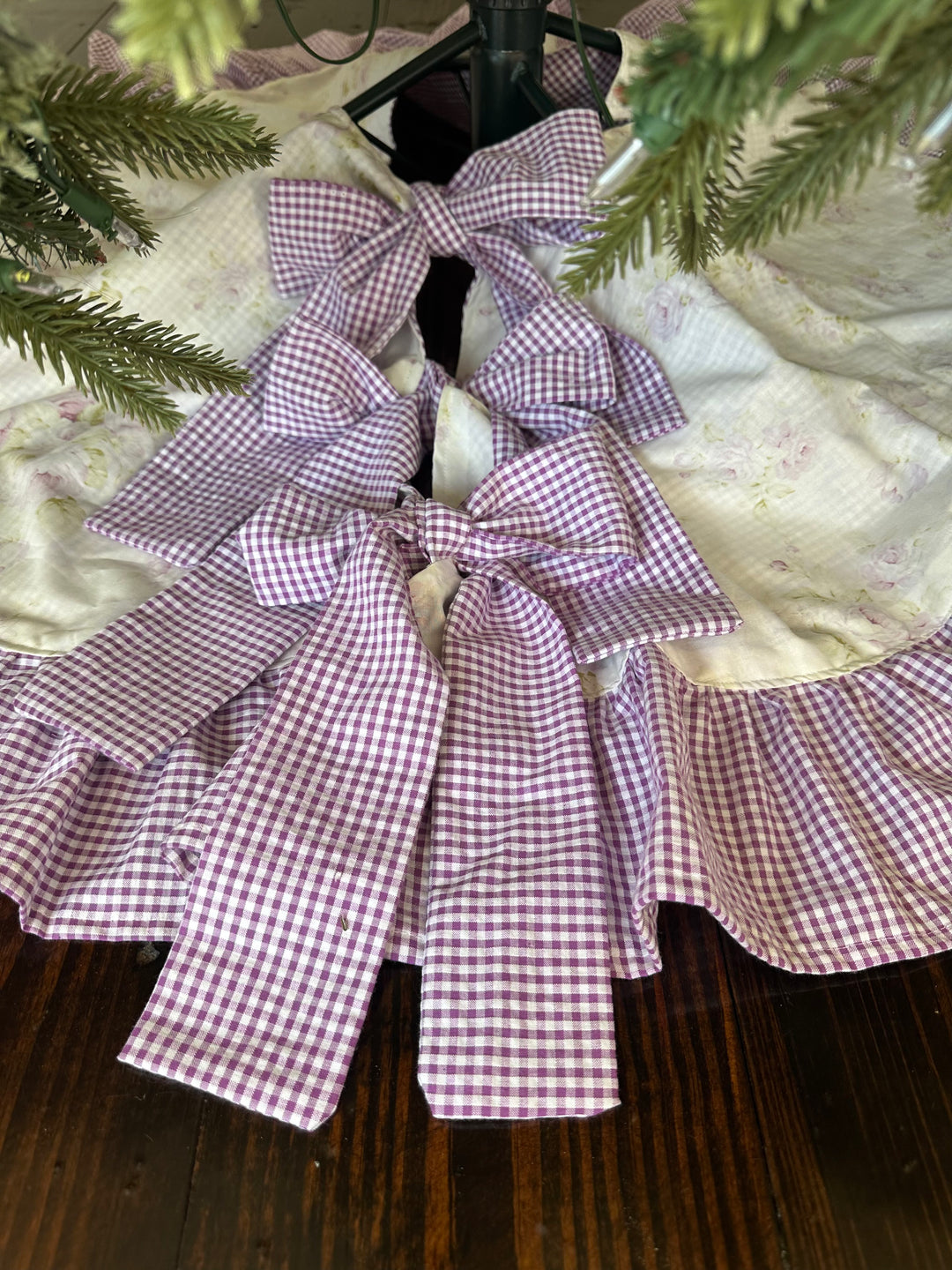 Lavender shabby chic floral Christmas tree skirt under a green tree, three lavender gingham sash ties knotted into bows at the front