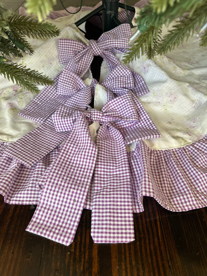 Lavender shabby chic floral Christmas tree skirt under a green tree, three lavender gingham sash ties knotted into bows at the front