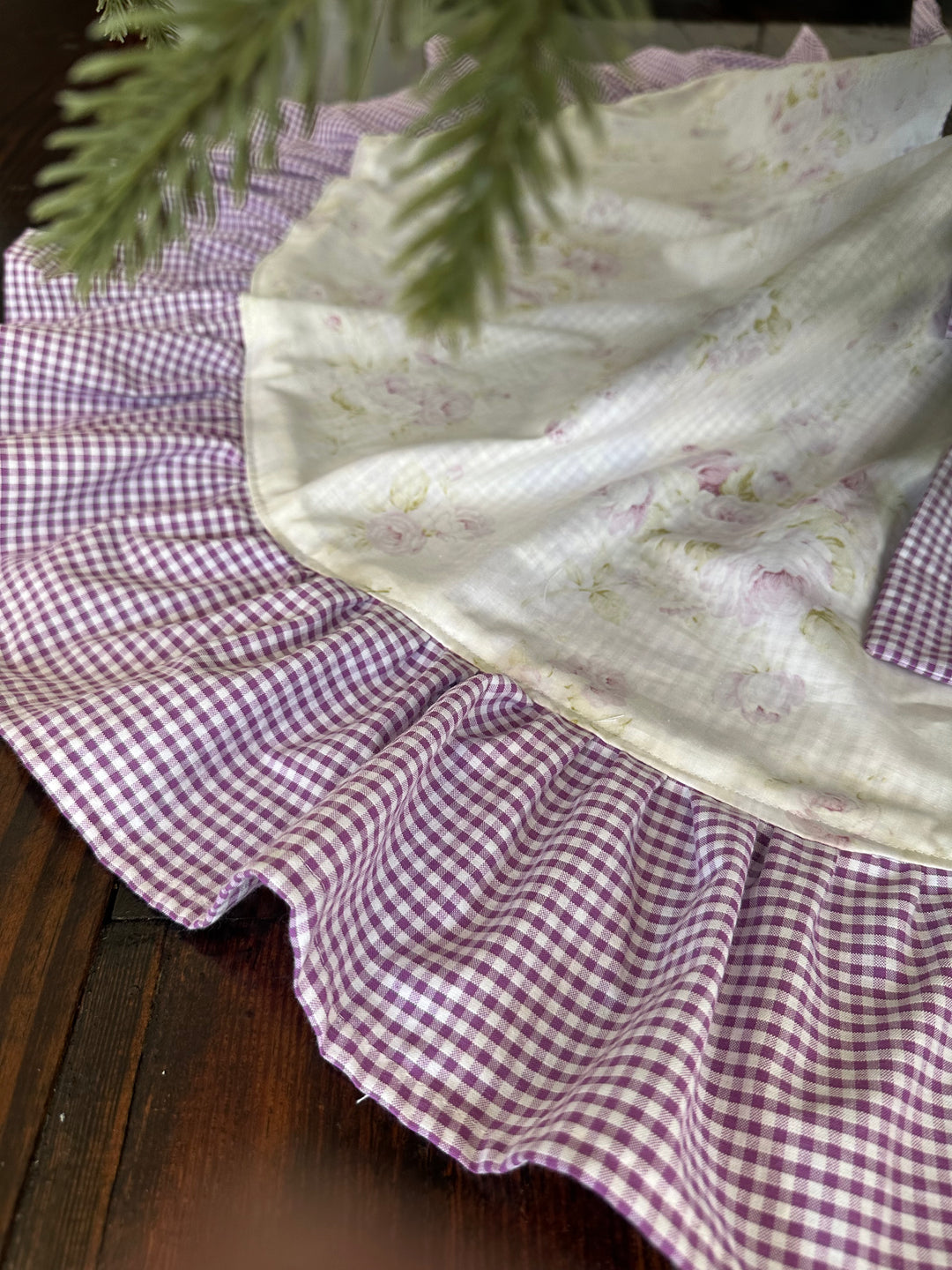 Side view of the floral tree skirt's edge with the full lavender gingham ruffle draped over wood planks