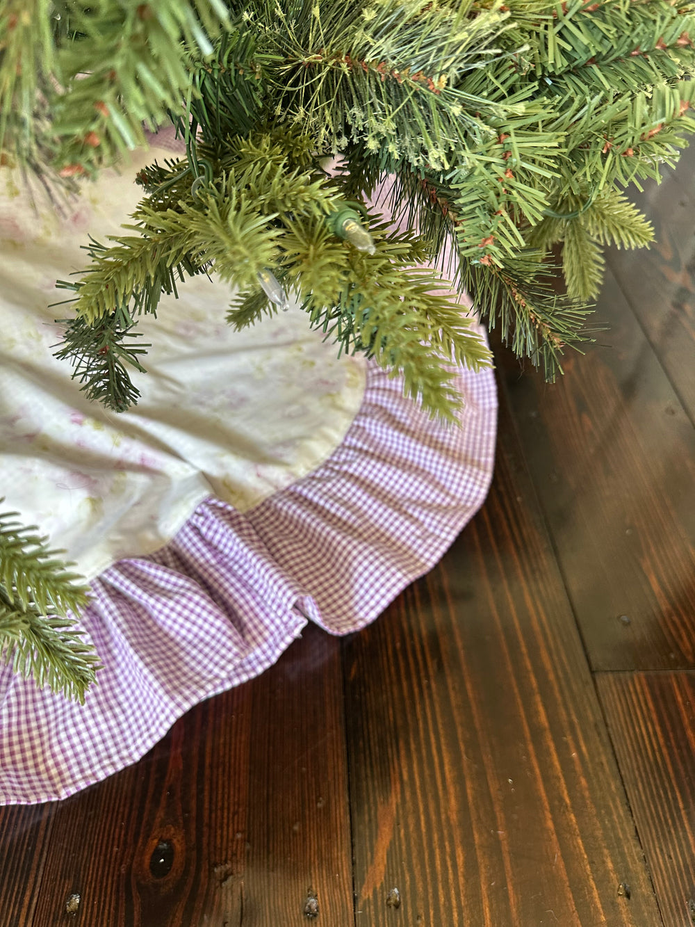 Lavender gingham ruffle peeking out from under the branches of a lit Christmas tree on a dark wood floor