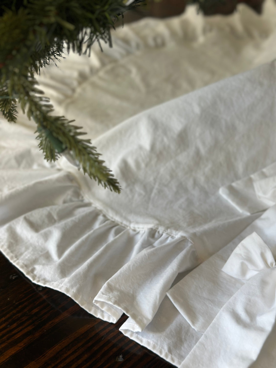 Soft washed-cotton texture of the white tree skirt and its ruffle under evergreen branches
