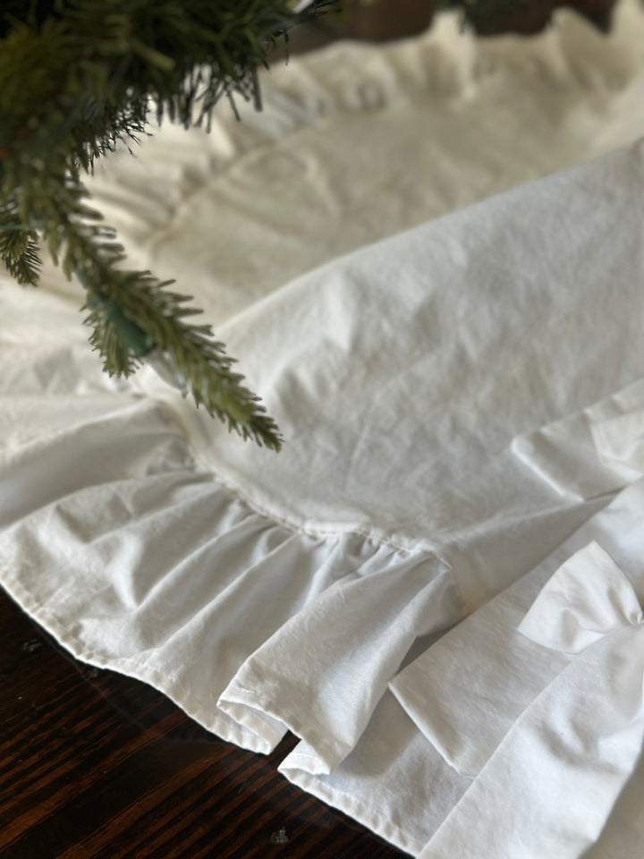 Soft washed-cotton texture of the white tree skirt and its ruffle under evergreen branches