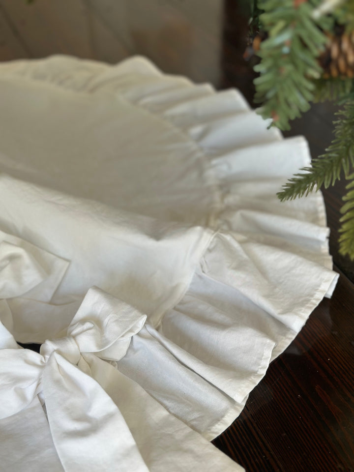 White bow tie resting on the gathered ruffle edge of the round cotton tree skirt