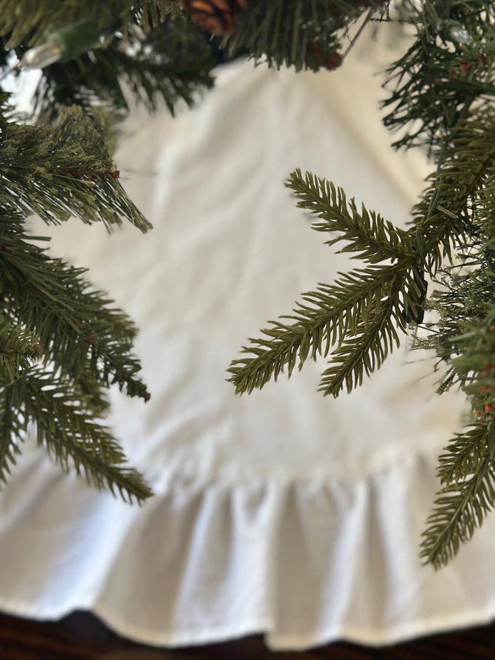 White tree skirt seen through blurred evergreen needles, the ruffle circling the base