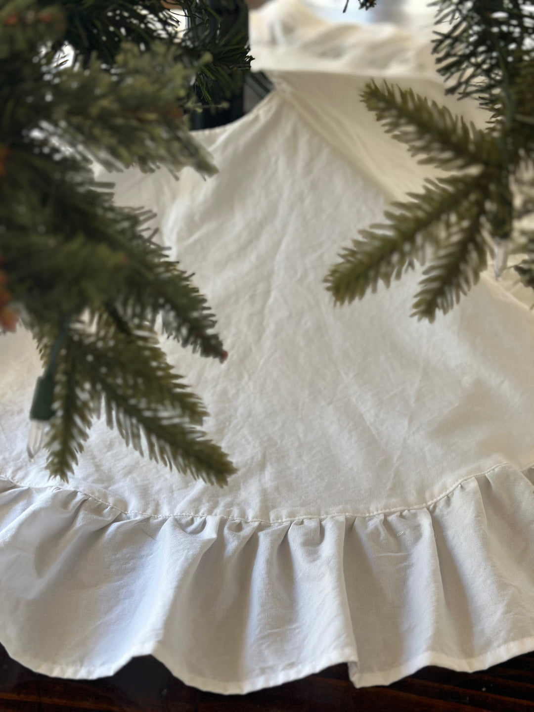 Green branches hanging over the smooth white body and ruffled hem of the tree skirt