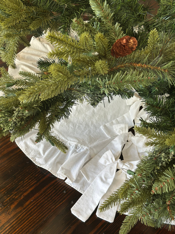 Looking down through pine branches and a pinecone at the white tree skirt and its bow ties