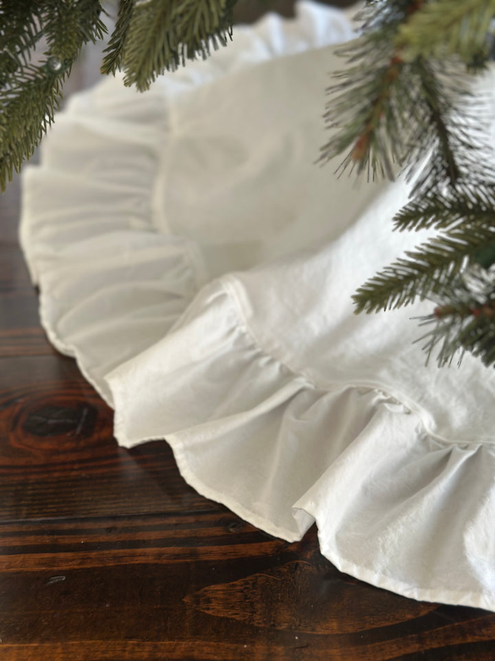 Sweep of the white gathered ruffle curving around the edge of the tree skirt on a wood floor