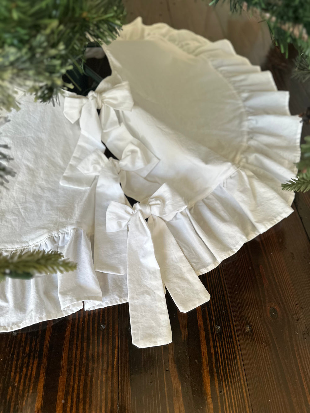 White cotton ties knotted into bows down the tree skirt opening, the full ruffle spilling onto a dark wood floor