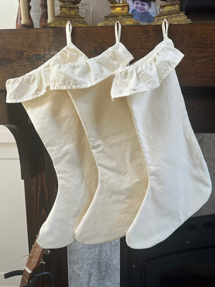 Three ivory farmhouse ruffled Christmas stockings hanging in a row from a dark wood mantel