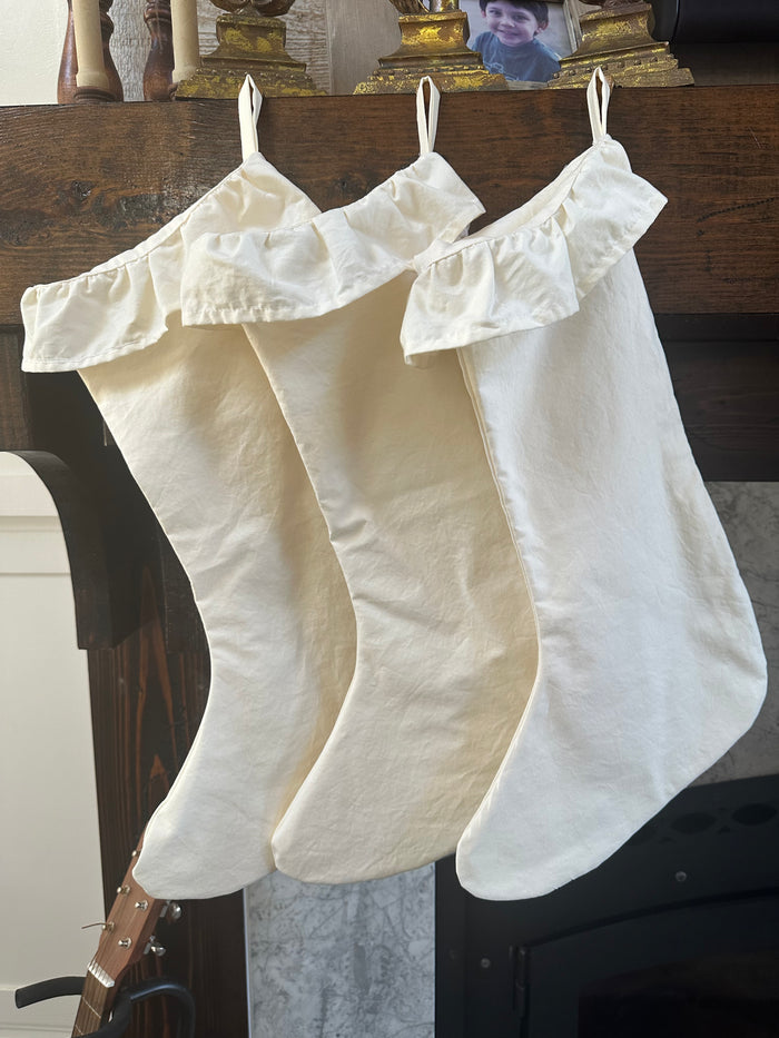 Three ivory farmhouse ruffled Christmas stockings hanging in a row from a dark wood mantel
