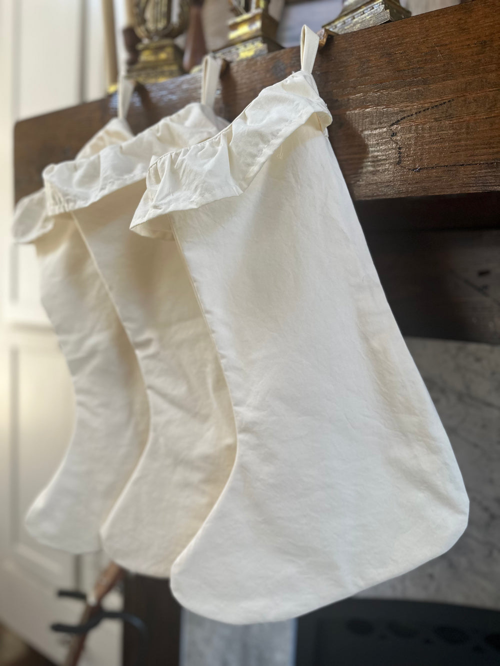 Angled view of three ivory cotton stockings on the mantel, ruffled cuffs catching the light