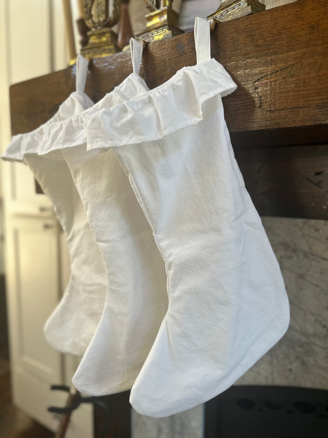 White ruffled stockings hanging in a row from cotton loops, seen from the side of the mantel