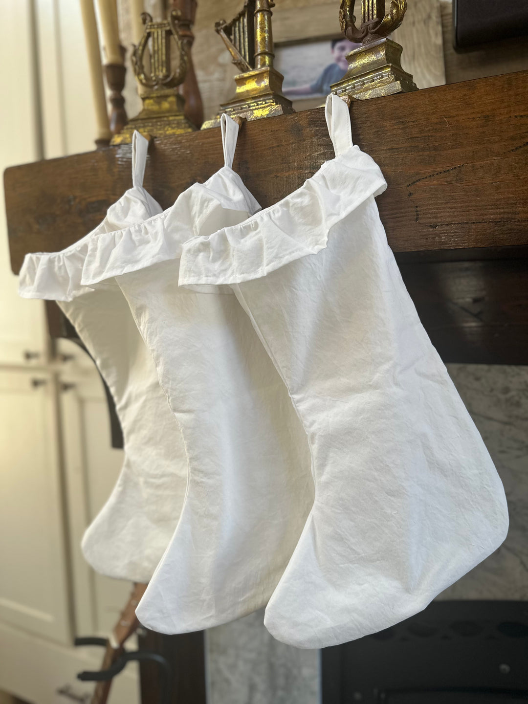 Matching white ruffled stockings for the whole family hung on a rustic mantel by the window