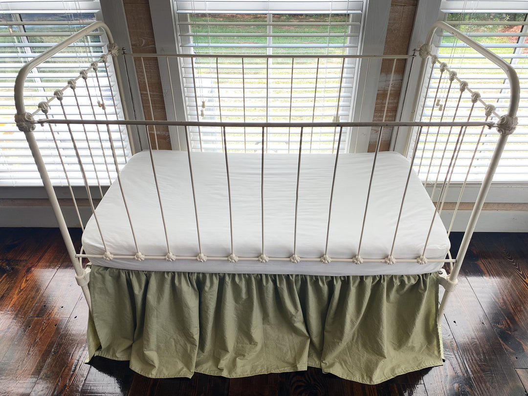 Close-up front detail of sage green gathered crib skirt showing soft ruffle and gather at mattress level