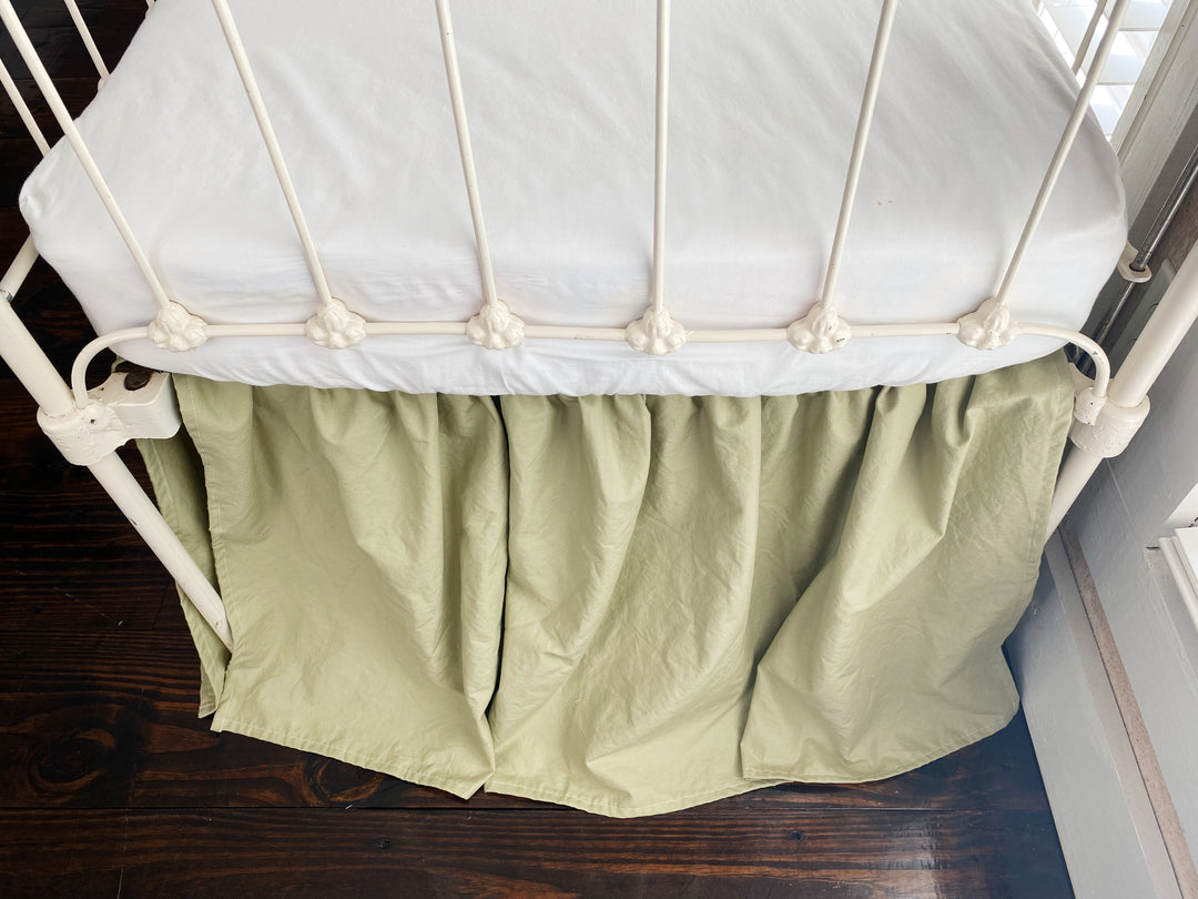 Side corner detail of sage green gathered crib skirt with split corner around white iron crib post, 20 inch drop