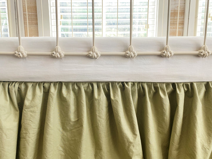 Close-up front detail of sage green gathered crib skirt showing soft ruffle and gather at mattress level