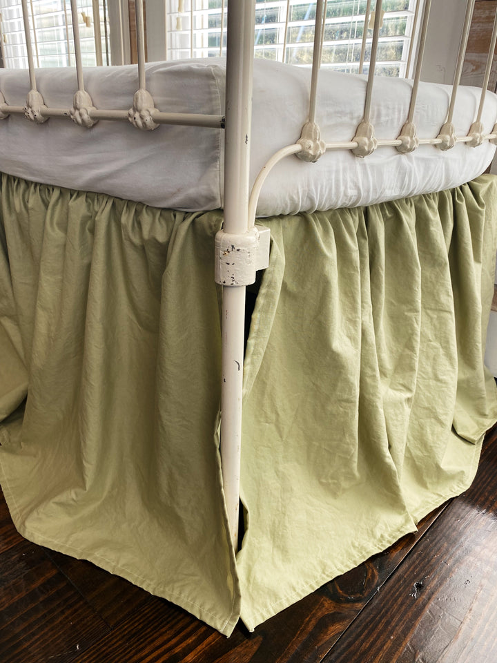 Side corner detail of sage green gathered crib skirt with split corner around white iron crib post, 20 inch drop
