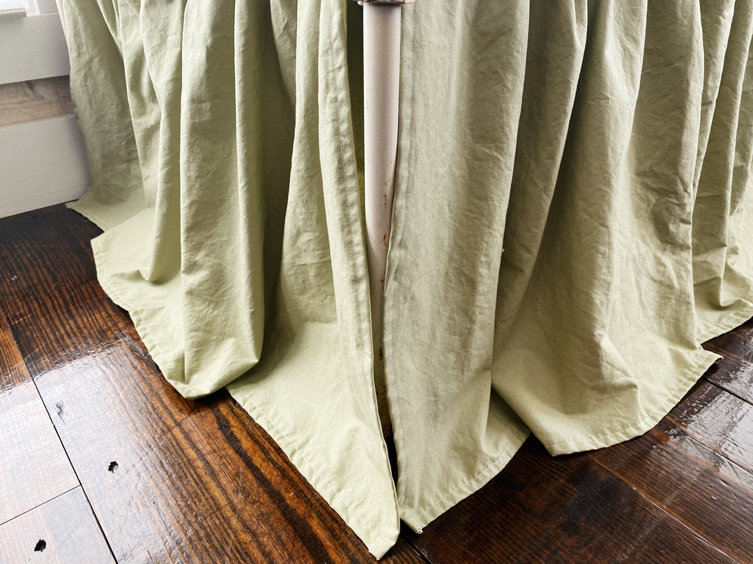 Close-up top-down view of sage green crib skirt gather detail where skirt meets mattress, washed cotton texture