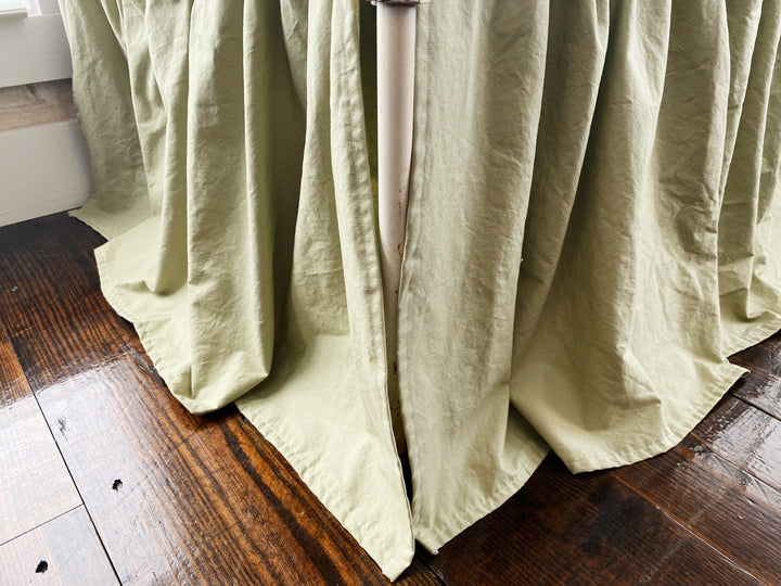 Close-up top-down view of sage green crib skirt gather detail where skirt meets mattress, washed cotton texture
