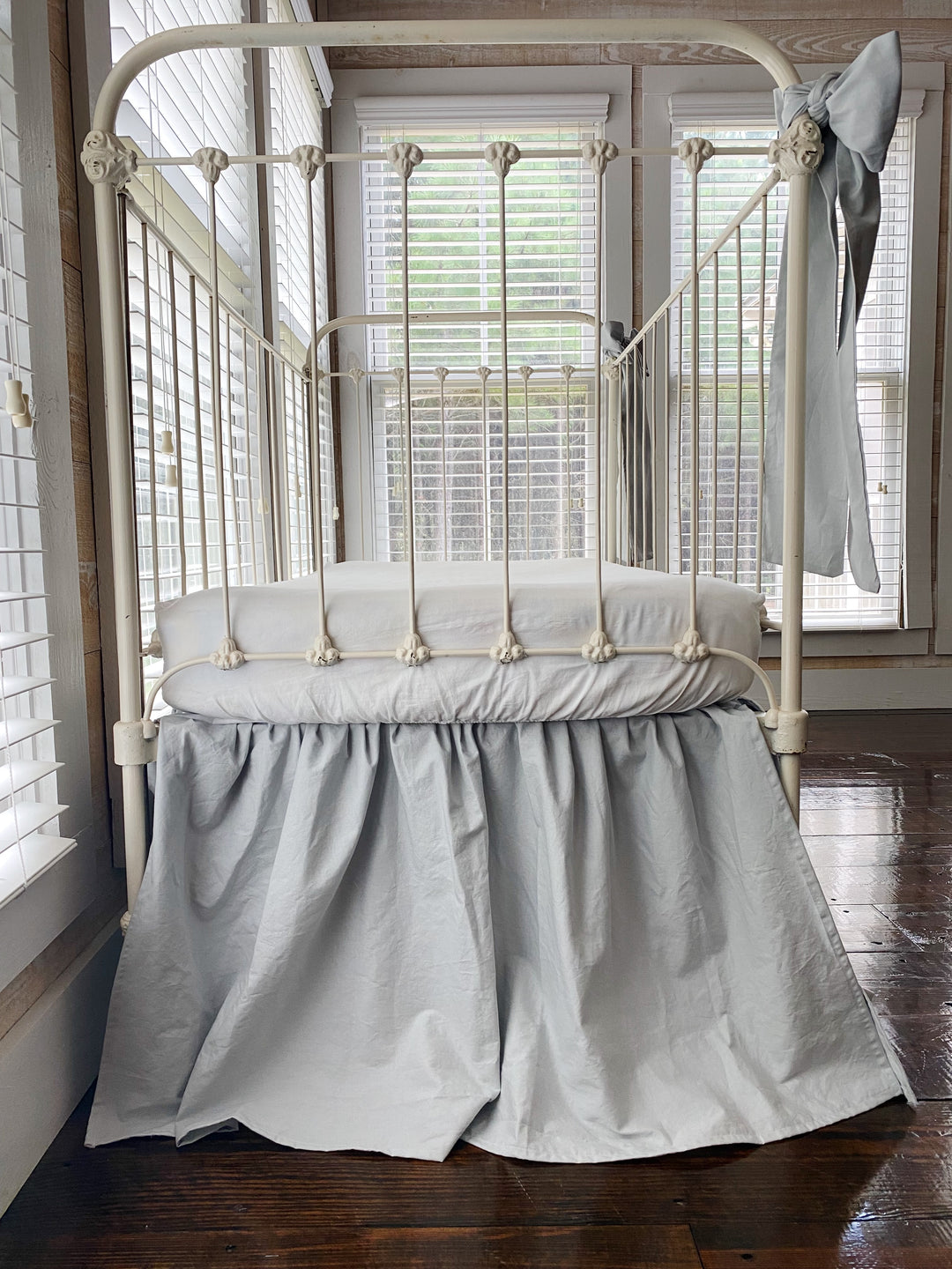 Zen grey 4-sided gathered crib skirt with two large bow set on antique white iron crib, full front view