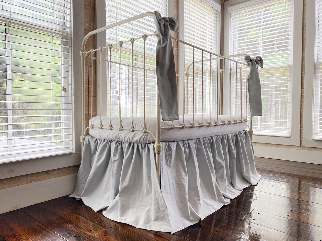 Zen grey gathered crib skirt on white iron crib, end view showing 20 inch drop and relaxed farmhouse silhouette