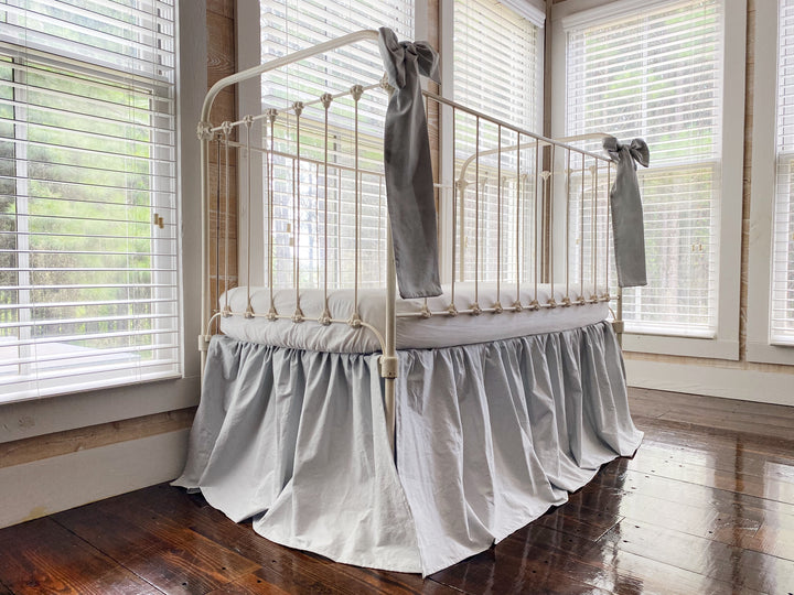 Zen grey gathered crib skirt on white iron crib, end view showing 20 inch drop and relaxed farmhouse silhouette
