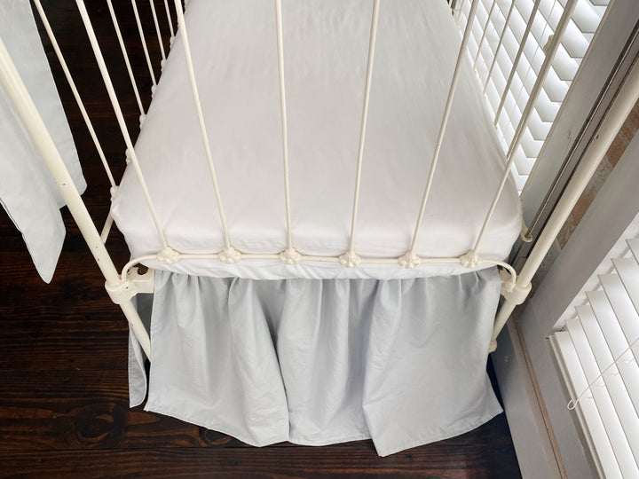 Top-down close-up of zen grey crib skirt gather detail meeting white mattress edge, washed cotton texture
