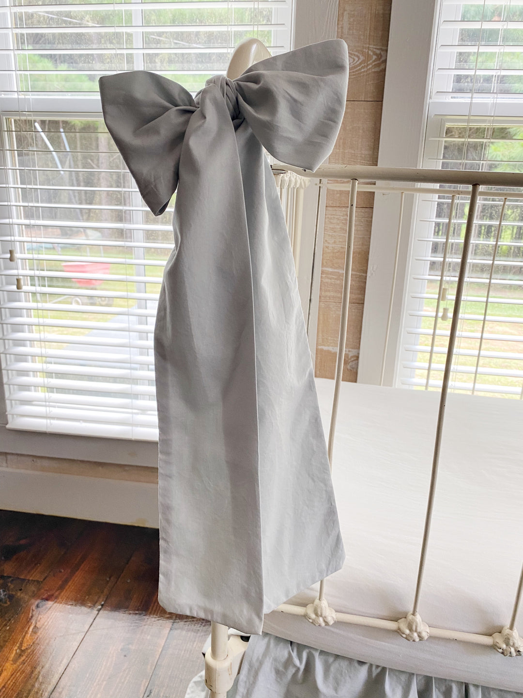 Overhead view of zen grey gathered crib skirt and large bow set with white fitted sheet, neutral nursery bedding