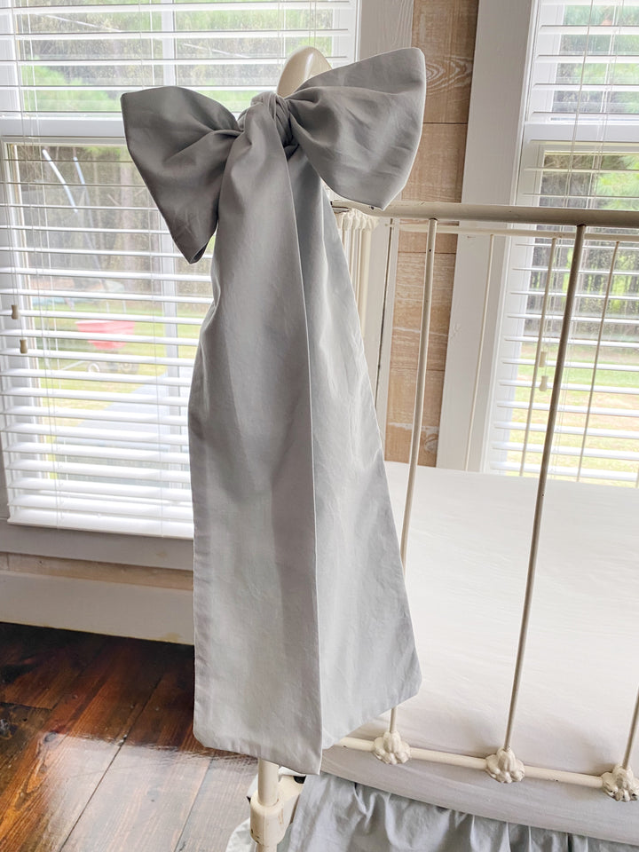 Overhead view of zen grey gathered crib skirt and large bow set with white fitted sheet, neutral nursery bedding