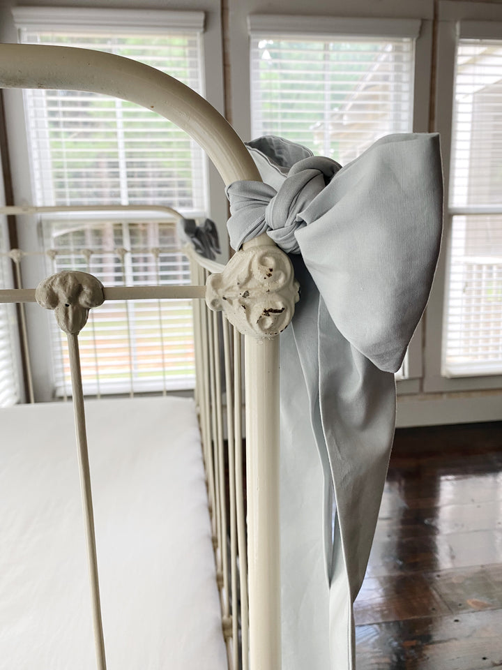 Detail close-up of large zen grey washed cotton crib bow knotted around ornate white iron crib post