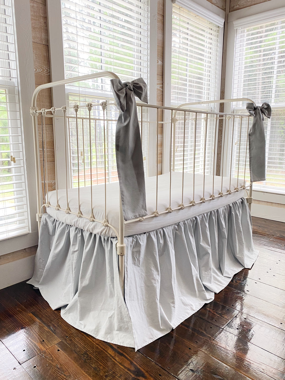 Zen grey crib skirt and large bow set, full three-quarter view on iron farmhouse crib, soft gray nursery bedding