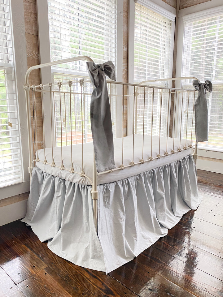 Zen grey crib skirt and large bow set, full three-quarter view on iron farmhouse crib, soft gray nursery bedding