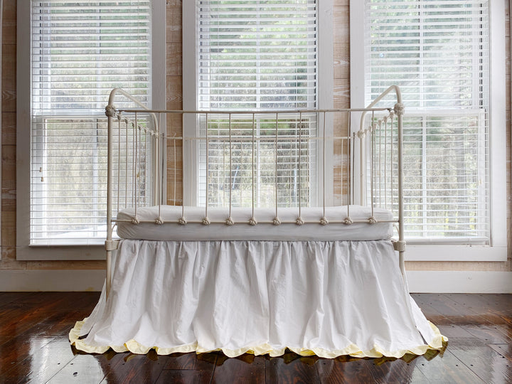 White and baby yellow ruffled crib skirt on white iron farmhouse crib, full front view in bright window light
