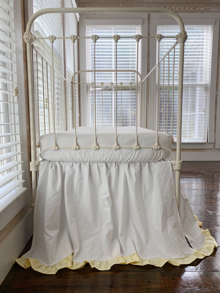 White and yellow two-tone ruffled crib skirt on iron crib, angled end view showing full gathered silhouette