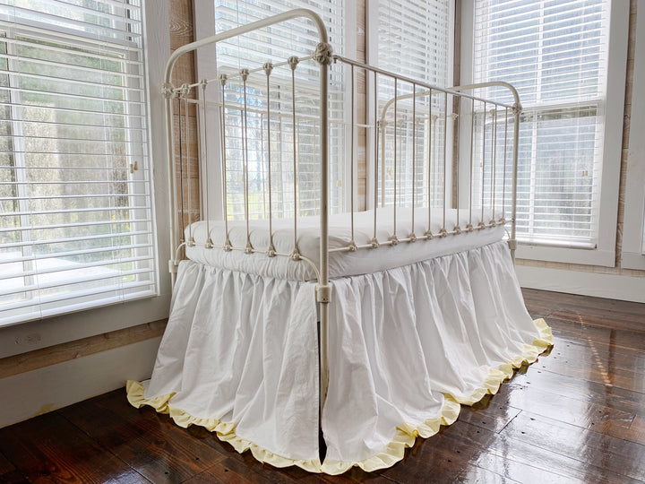 White and baby yellow ruffled crib skirt, three-quarter angle view on iron farmhouse crib in bright nursery