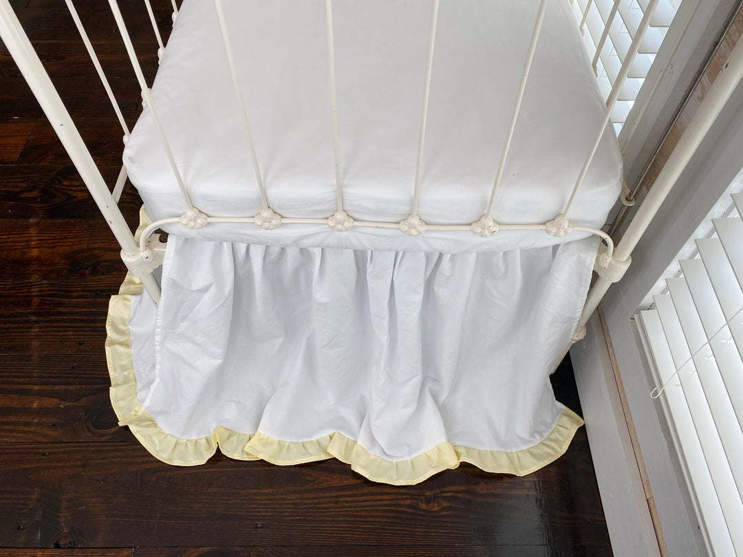 Top-down close-up of white and yellow ruffled crib skirt gather detail at mattress edge, washed cotton nursery bedding