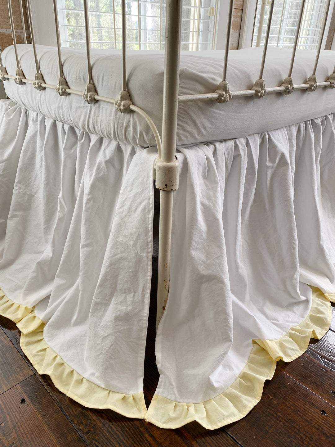Floor-level corner close-up of baby yellow ruffle hem on white gathered crib skirt, washed cotton heirloom nursery