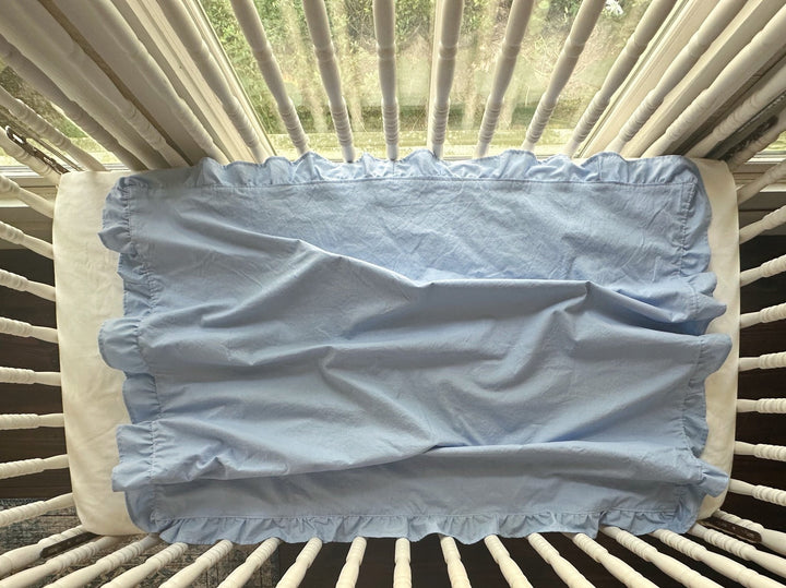 Overhead view of a baby blue ruffled crib blanket spread across a standard crib mattress - High Cotton Textile