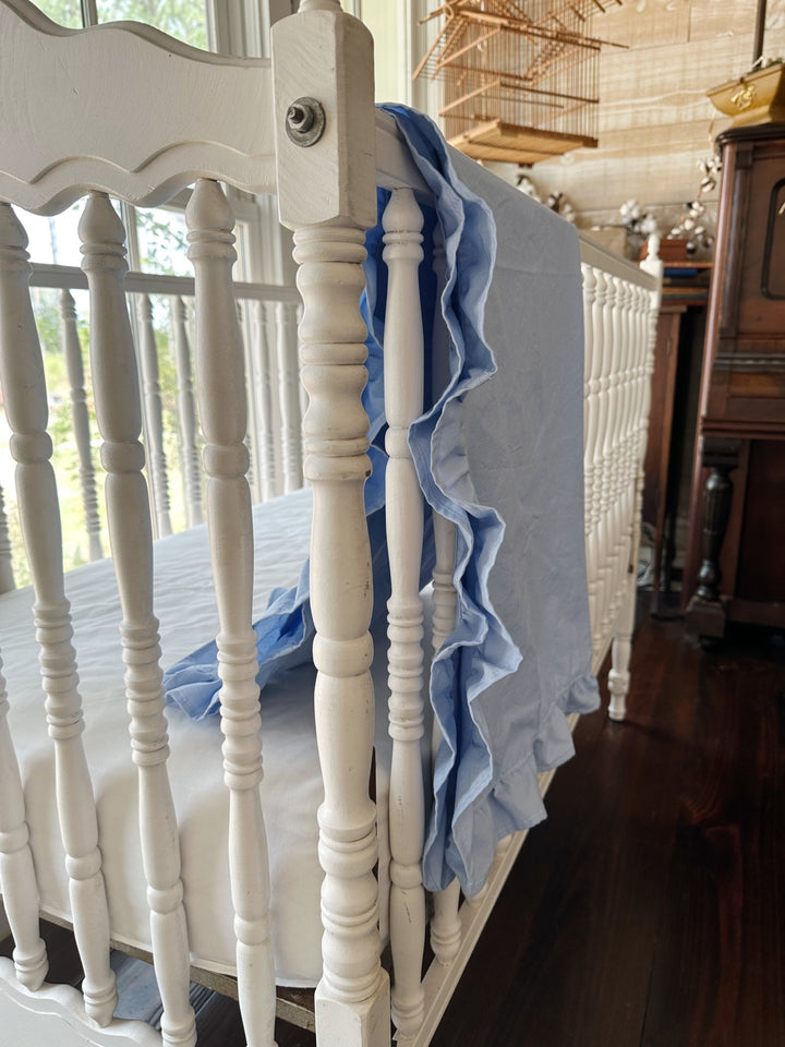 Light blue ruffled baby blanket draped over the end rail of an antique crib, ruffle falling in soft folds - High Cotton Textile