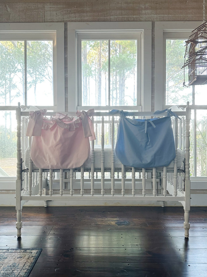 Baby blue tailored caddy hanging beside the baby pink ruffled caddy on a white crib