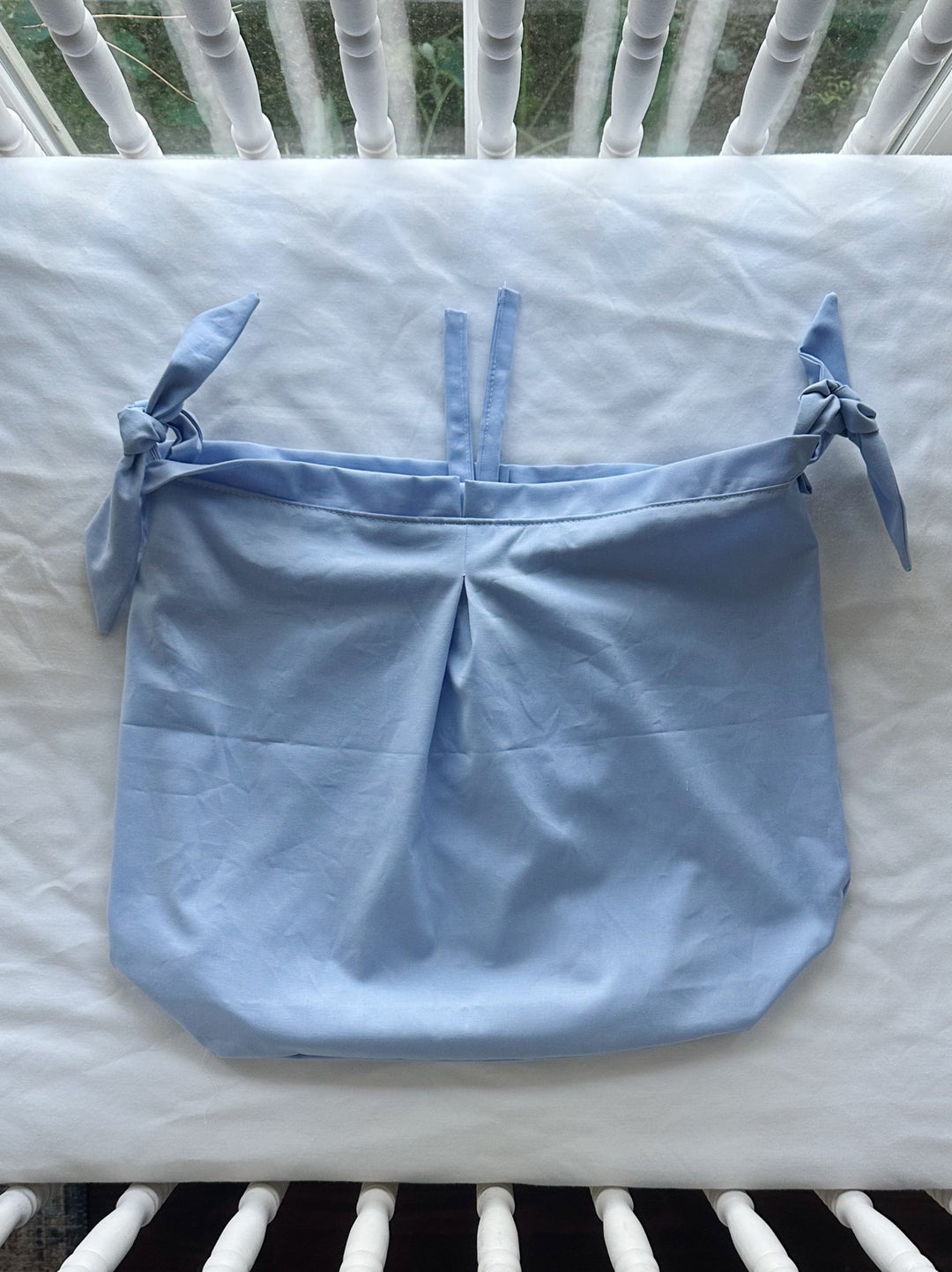 Baby blue tailored crib caddy laid flat, showing the center box pleat and the ties at each end