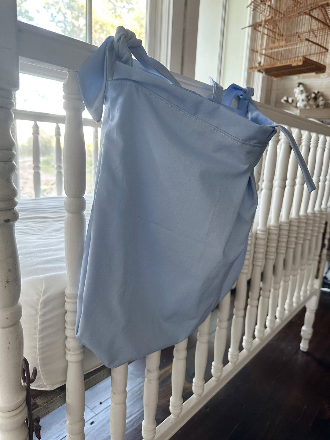 Side view of the baby blue caddy hanging from the crib rail, a knotted tie at the corner